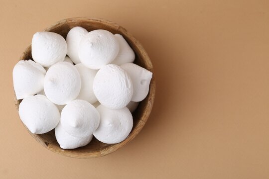 Delicious meringue cookies in bowl on beige background, top view. Space for text