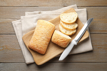 Fresh crispy ciabattas and knife on wooden table, flat lay