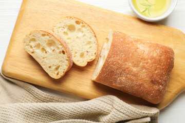 Fresh crispy ciabatta and oil with rosemary on white wooden table, flat lay