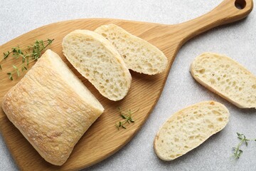 Cut crispy ciabatta and thyme on light grey table, flat lay