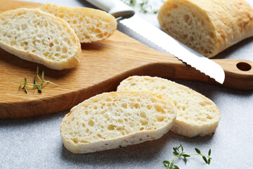 Pieces of crispy ciabatta, knife and thyme on light grey table, closeup