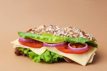 Tasty ciabatta sandwich with cheese and vegetables on brown background, closeup