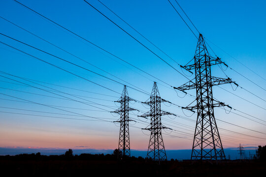 three metal poles of high-voltage power lines against the sunset