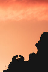 A couple is sitting on a rock and looking at their cell phones