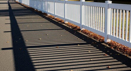 Obraz premium Shadows on a Paved Path Beside a White Fence