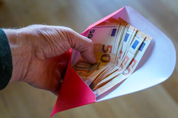 Hand holding envelope filled with fifty euro banknotes, concept of savings, salary or financial gift
