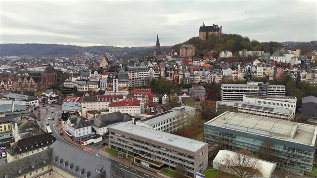 Aerial view of Marburg cityscape in Hesse, Germany, showing the Landgrafenschloss Castle on the hill, historic old town, and modern architecture under cloudy skies