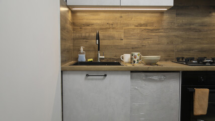Modern kitchen sink with black faucet, cups, plates and soap dispenser on wooden countertop; cozy domestic lifestyle and clean interior design concept