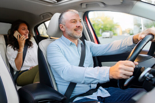 Woman passenger talking on cellphone sitting on backseat in taxi, cheerful male driver riding car with smile. Taxi service concept