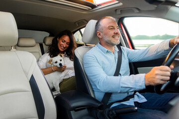 Cheerful man taxi driver riding car with woman sitting in backseat with her dog. Pet friendly taxi service