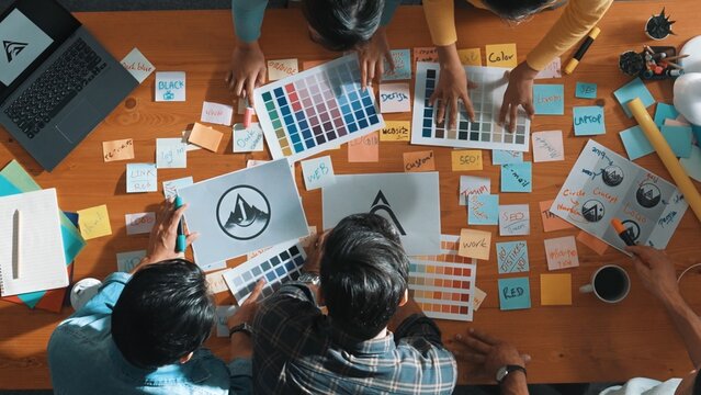 Top down view of smart designer explain and brainstorming idea for logo design and writing concept. Aerial view of business people discuss and talking while using sticky notes sharing idea. Symposium. - Powered by Adobe