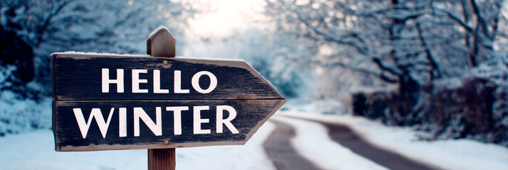 Wooden arrow sign with text hello winter on snowy road background, winter forest landscape with frosted trees and seasonal atmosphere