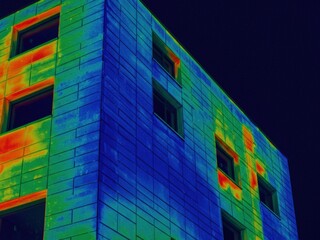 Thermal image of a building facade displaying heat distribution with cool blues/greens and warm oranges/reds around windows, suggesting energy analysis.