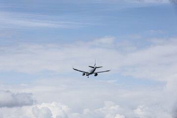 Airplane approaching airport runway under cloudy blue sky with engines visible and wings extended for landing