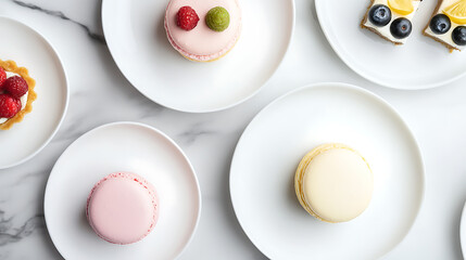 Fototapeta premium Overhead view of assorted fruit tarts and macarons arranged on white plates, showcasing colorful and delicate pastries against a white marble backdrop.