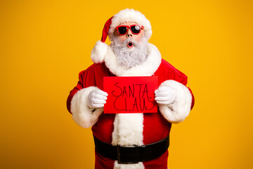 Santa Claus posing with sunglass displaying a festive sign against a vibrant yellow background