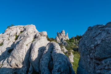 Jagged white limestone peaks rise towards a clear, deep blue sky on a sunny day. This stunning karst landscape is a famous landmark for hikers and climbers in the Velebit mountains of Croatia.