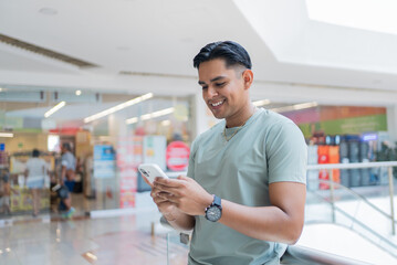 Happy mexican man using a smartphone in a shopping mall next to a department store