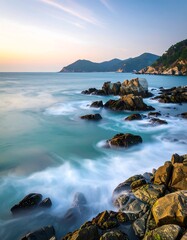 Obraz premium Coastal rocks at sunrise. Gentle waves caress large, dark rocks along a serene shoreline. Soft light paints the horizon