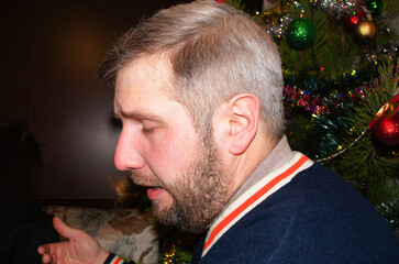 Middle aged man with beard looking down next to decorated christmas tree