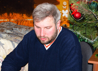 Middle aged man with beard looking down next to decorated christmas tree