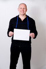 Smiling man in dark sporty clothes holding blank white sign for copy space