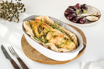 A freshly baked chicken breast roll is presented in a baking dish, adorned with herbs, alongside a...