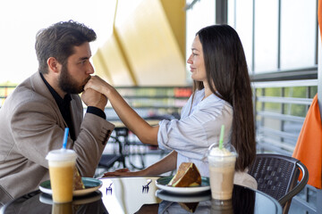The man is kissing the woman's hand while they are sitting at a table together