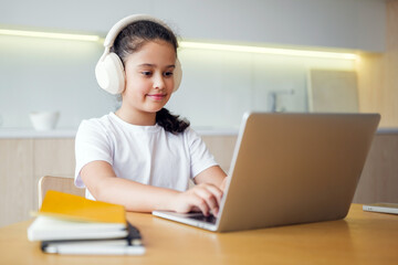 Young girl uses laptop while wearing headphones in modern workspace