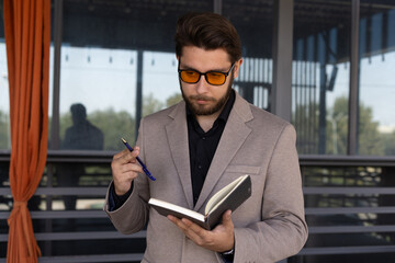 The man is holding an open notebook and a pen, appearing to be writing 