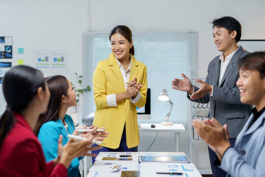 Asian business professionals collaborating, recognizing success during a presentation in a modern office, celebrating teamwork and achievement