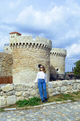 Fototapeta premium A female tourist admires the architecture of the Belgrade Fortress near the Zindan Gate. Concepts of balanced travel lifestyle, slow exploration habits, and wellness-oriented cultural experiences.
