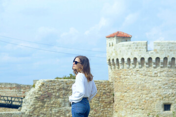 A woman stands near ancient wall against the backdrop of a medieval tower with machicolations....