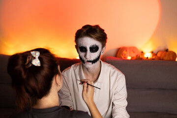 A woman is applying makeup to a man for Halloween party.