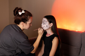 Woman painting girl's face with intricate designs, both smiling