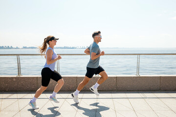 Obraz premium Couple jogging along waterfront path on sunny day near city skyline