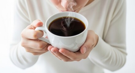 Person holding a steaming cup of coffee, bringing it close to their face.