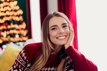 Cheerful woman in red sweater relaxing at home beside a twinkling christmas tree with cozy decor...