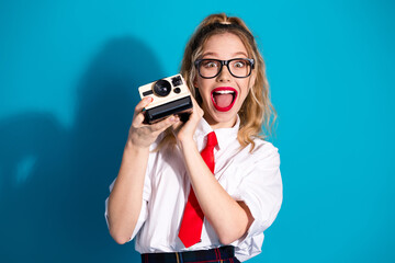 Cheerful young woman in stylish uniform holding retro camera on blue background