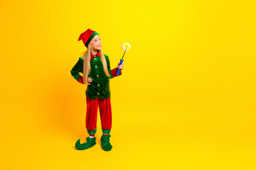 Festive girl dressed in a vibrant elf costume creating a joyful holiday vibe on a yellow background for Christmas