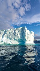 Iceberg rising above calm waters under a partly cloudy sky