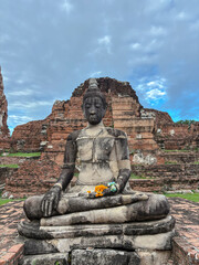 Old buddha sculpture with offerings on a ruined temple in Ayutthaya, Thailand