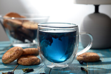 Blue butterfly pea tea in glass cup with cookies on blue wooden table