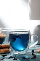Blue butterfly pea tea in glass cup with cookies on blue wooden table