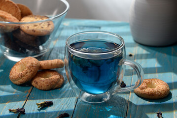 Blue butterfly pea tea in glass cup with cookies on blue wooden table