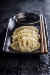Traditional japanese gyoza dumplings, chopsticks and soy sauce on black table.