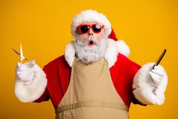 Festive Santa Claus in a barber role with a red costume, holding scissors and a comb, on a vibrant yellow backdrop