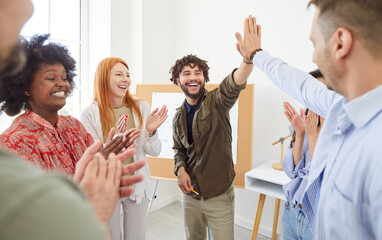Multiracial team of happy young people applauding, celebrating success after business meeting or...