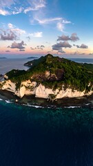 Aerial view of a tropical island at sunset.  Coastal cliffs meet turquoise water.  Dramatic clouds fill the sky