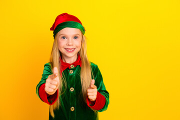 Playful child dressed as a Christmas elf in vibrant green outfit, smiling joyfully on bright yellow background, adding festive cheer